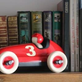 Red toy racing car on bookshelf in front of books