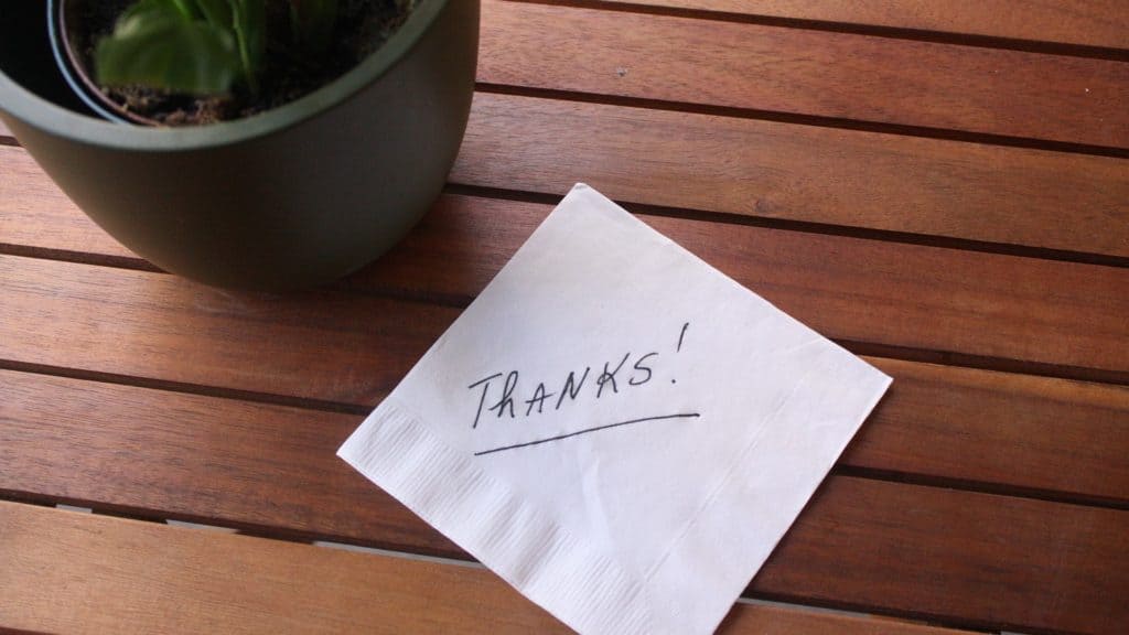 The word 'thanks' written on a napkin on a wooden table