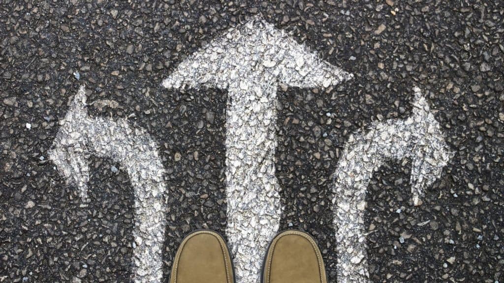 Toes of brown shoes on three white chalk arrows on road