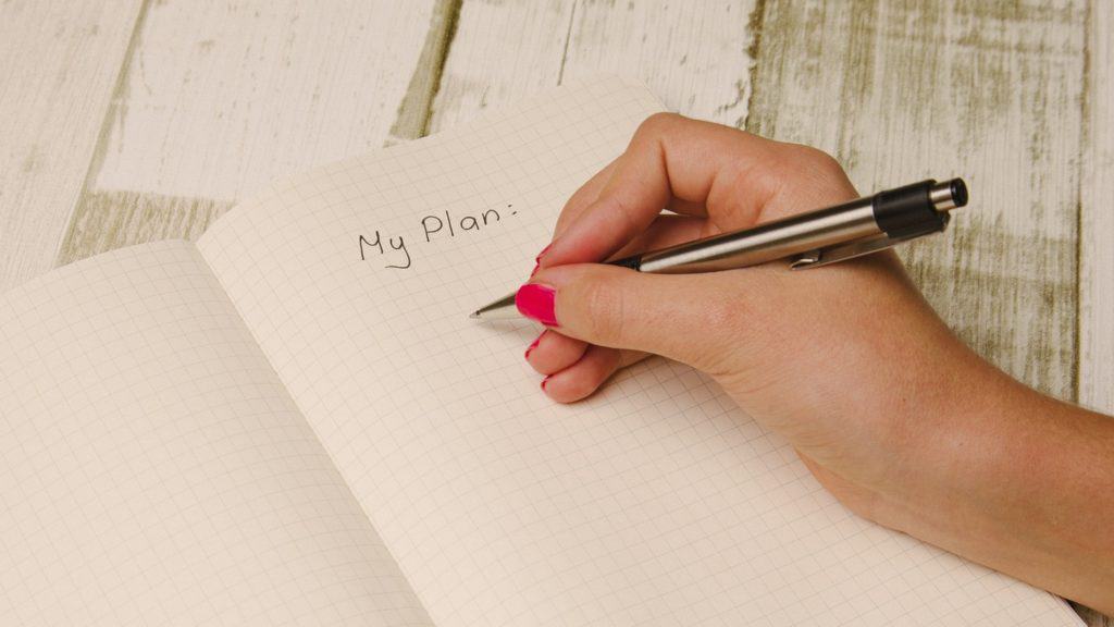 Hand holding pen over a notebook with words 'My Plan'