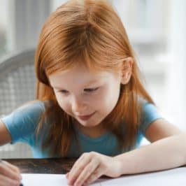 Young girl sat at table writing