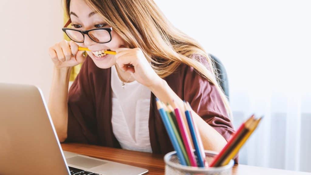 Woman biting pencil in frustration looking at laptop