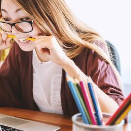 Woman biting pencil in frustration in front of laptop