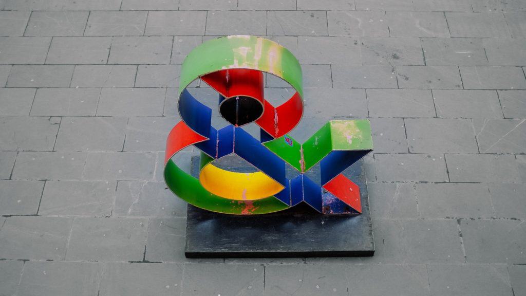 Colourful ampersand sculpture on grey pavement