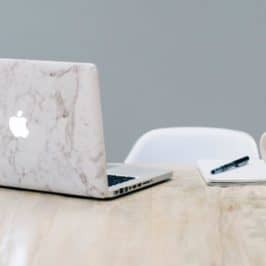 MacBook with marble cover design, pen on notepad and mug on table