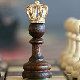 Brown wooden chess pawn piece wearing a crown