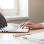 Close-up of woman's arm in a white blouse, her hand on a laptop