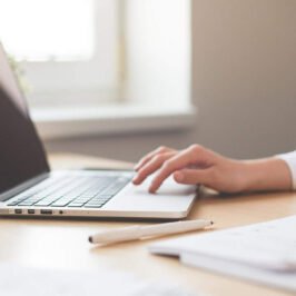 Close-up of woman's arm in a white blouse, her hand on a laptop