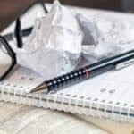 Screwed up ball of paper, glasses and pen on blank pad of paper