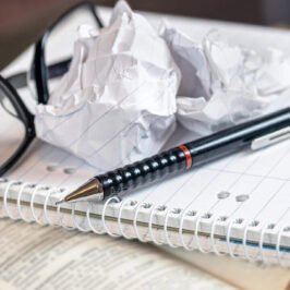 Screwed up ball of paper, glasses and pen on blank pad of paper